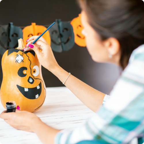 mulher pintando um balão laranja com as cores de uma abóbora 