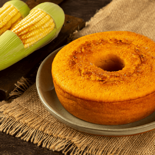 Imagem de um bolo de milho com dois milhos ao lado