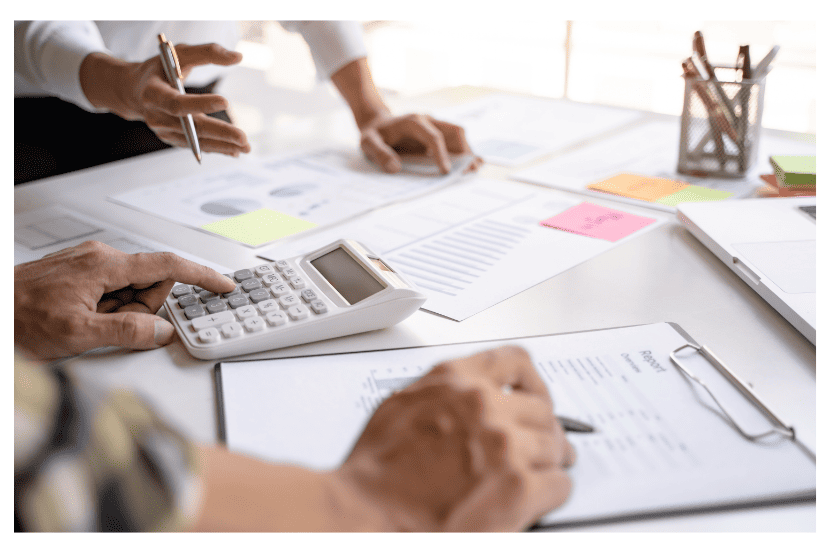 Imagem contendo uma mesa com papeis e uma calculadora sendo usada por uma pessoa. 