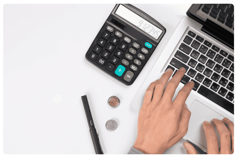 imagem tirada de cima. Uma mesa com calculadora e notebook, além de duas moedas e uma caneta. 